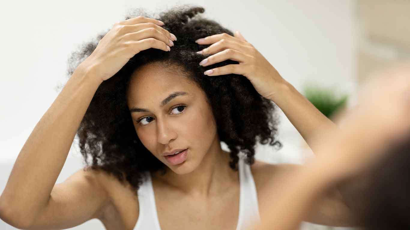 Vrouw staat voor een spiegel en onderzoekt haar hoofdhuid. 